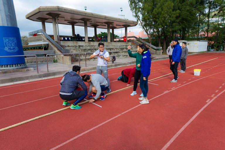 Group of people playing tug-of-war on a red running track.